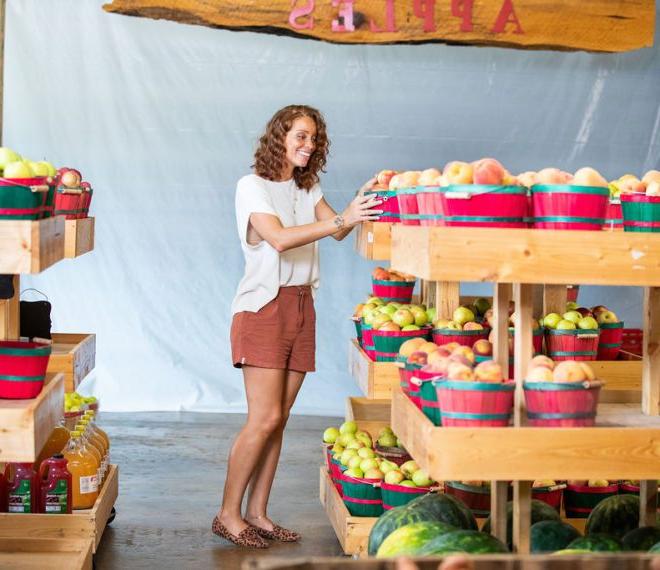 a woman browsing buckets of fresh peaches and apples
